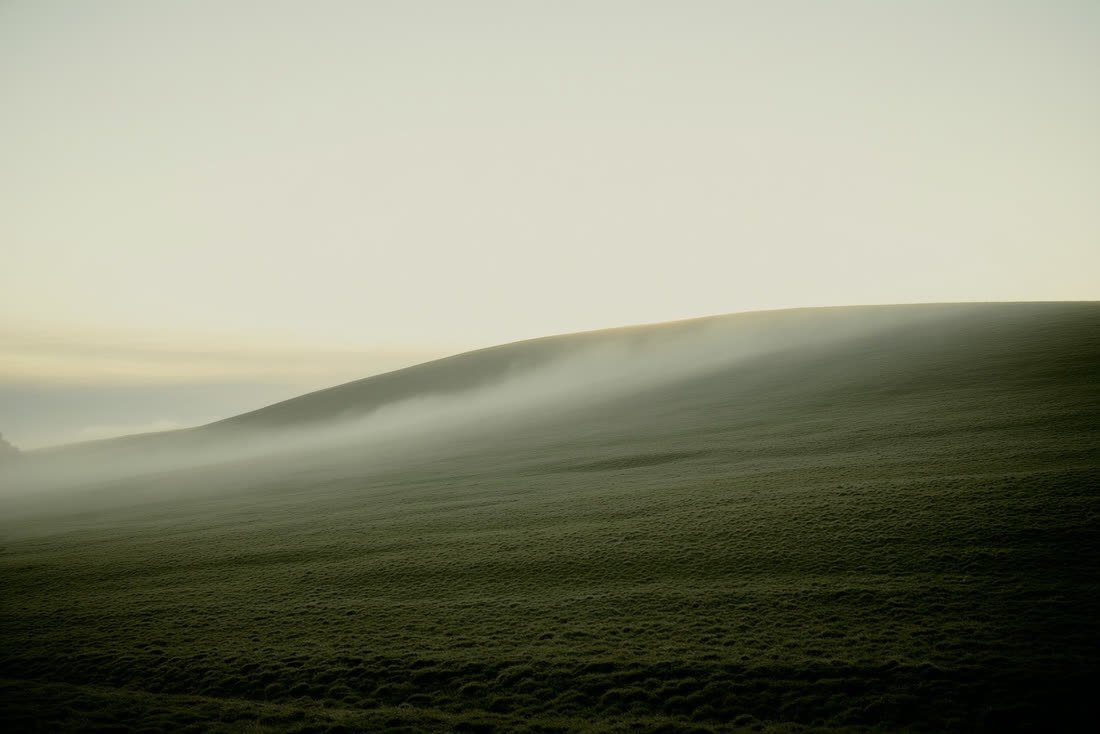 A low ridge at dawn with mist lifting off the slope as the land begins to clear